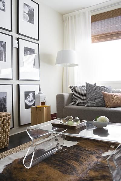 Chic modern living space! DWR Overstock acrylic coffee table, brown cowhide rug, gray modern sofa, black & white photo gallery, white floor lamp, bamboo roman shades, white drapes, black blue orange pillows and jute rug. LOVE the black and white pictu