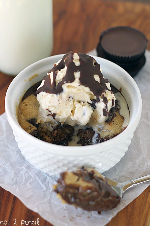A warm. decadent microwave chocolate chip cookie in a cup, stuffed with a Reese's peanut butter cup and topped with vanilla ice cream.